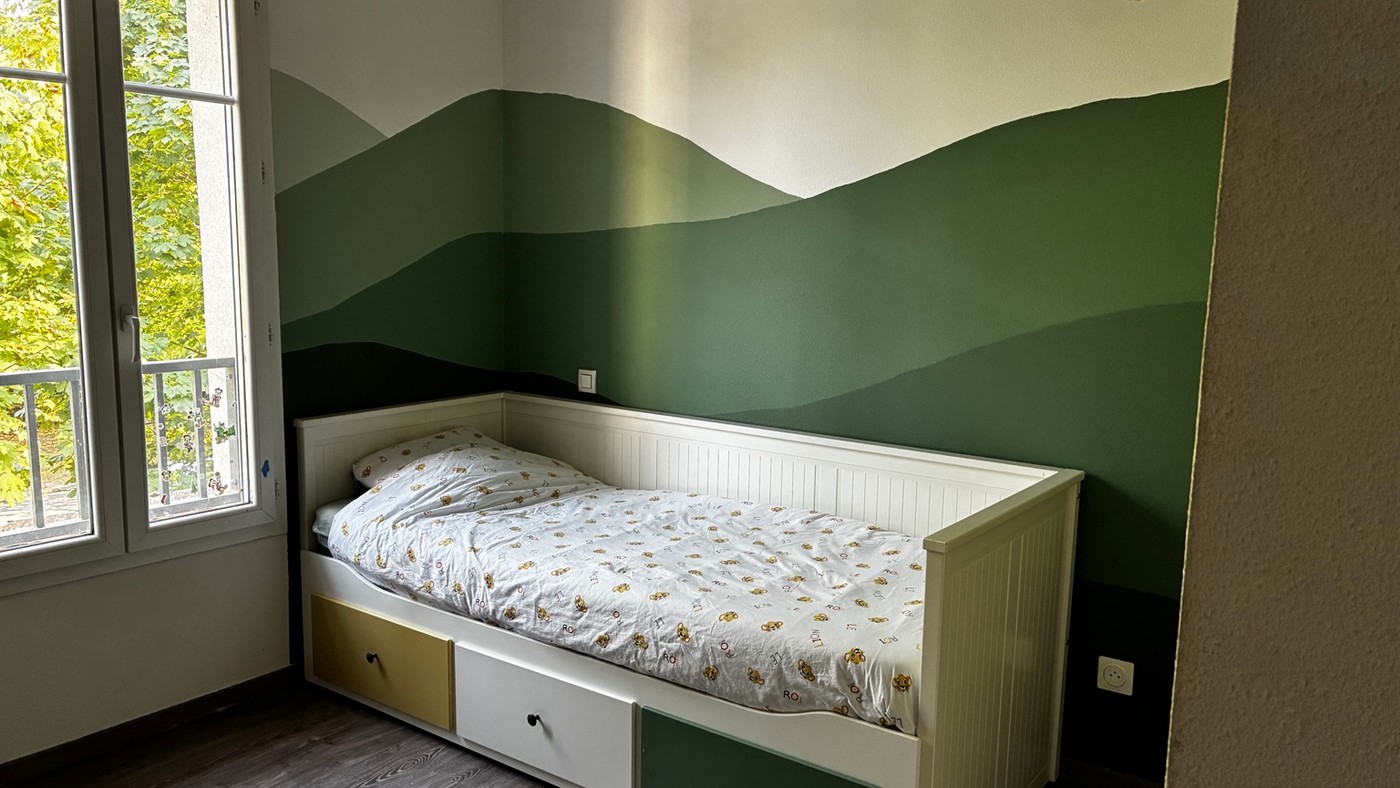 Chambre d’enfant avec lit extensible à tiroirs et paysage de montagnes peint dans plusieurs nuances de vert
