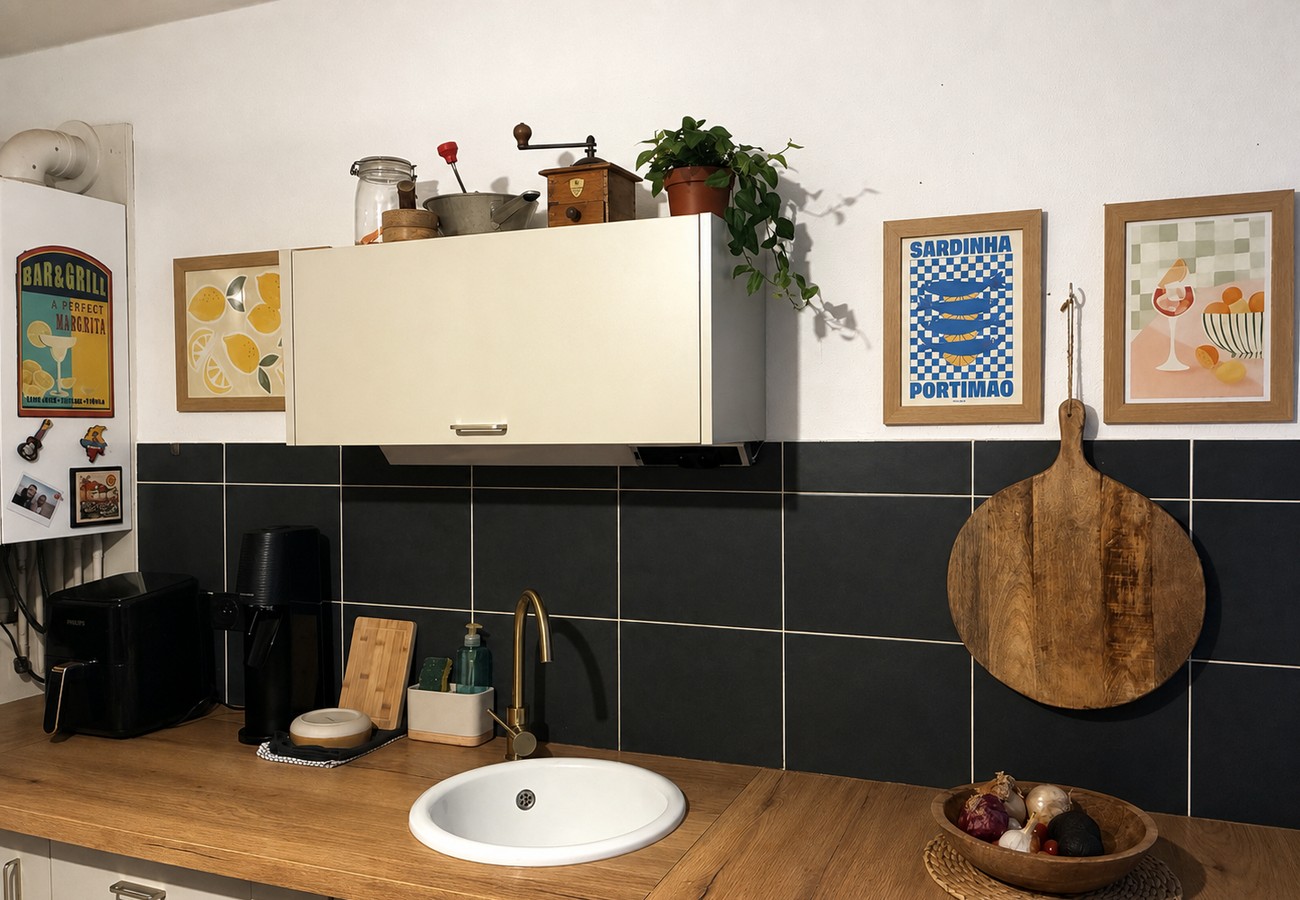 Vue élargie de la cuisine réelle avec évier rond, robinet en laiton, cadre Sardinha, plante et objets disposés au-dessus du meuble